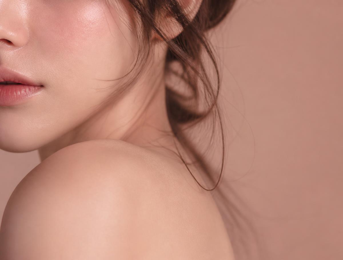 Soft editorial close-up of an adult woman's cheek and shoulder in warm light